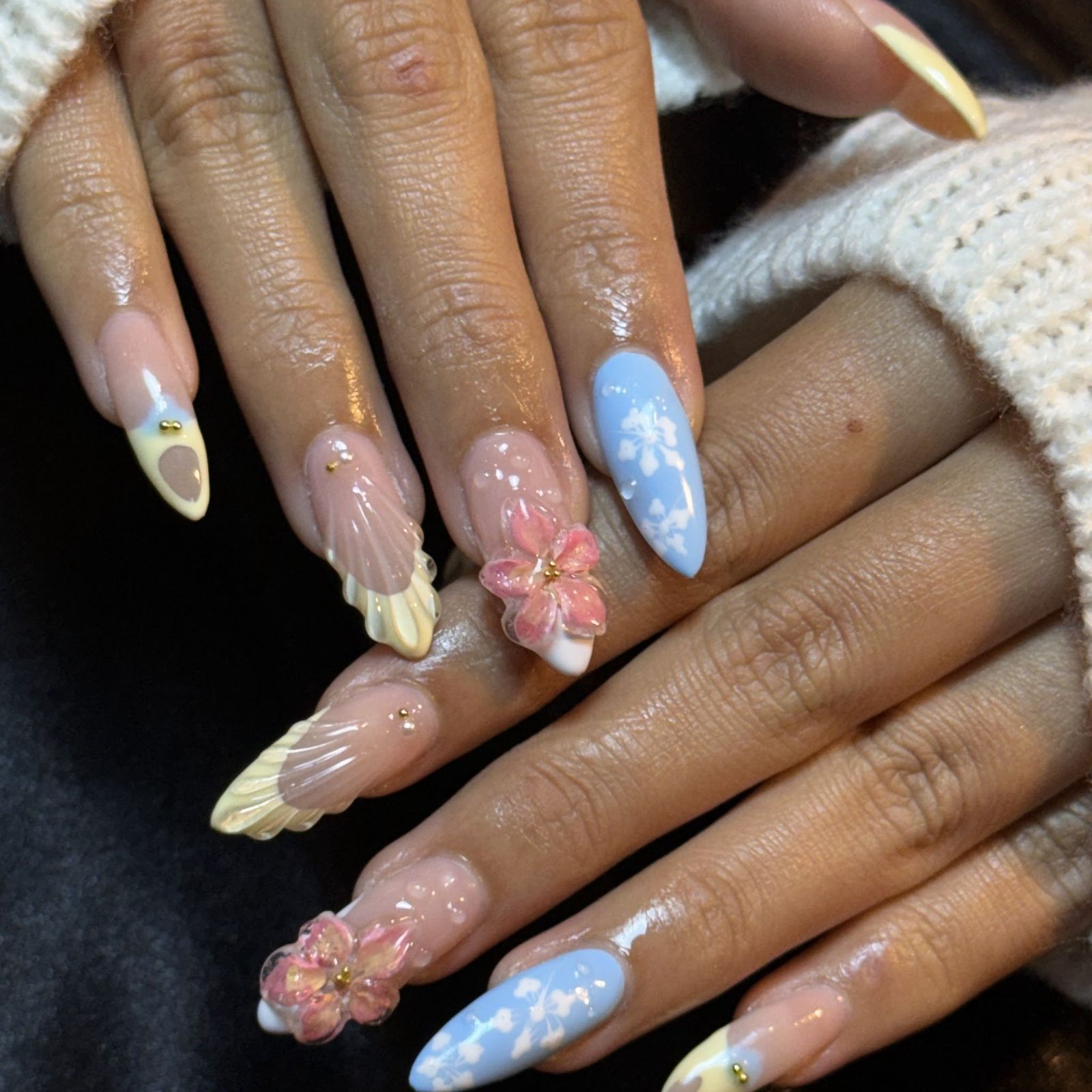 Lange amandelnagels met pastel 3D-bloemen, schelpjes en een blauwe bloemennagel