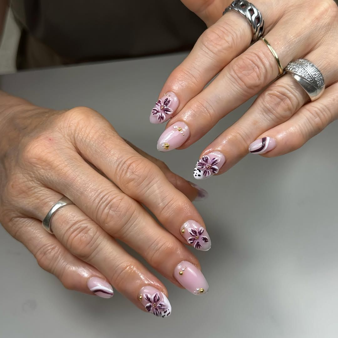 Handgeschilderde aubergine bloemen op nude amandelnagels